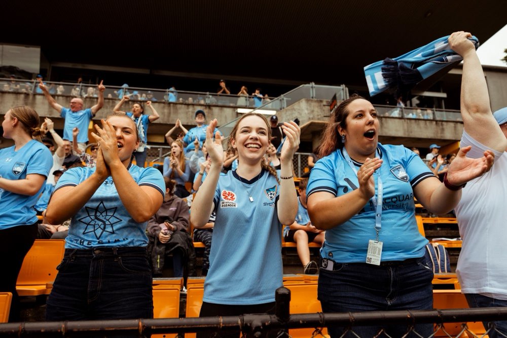 Sydney FC fans in sky blue jerseys clapping and cheering