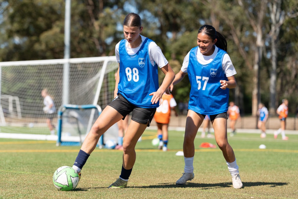 Two girls in blue Sydney FC training bibs working on the ball at a Female High Performance Camp session