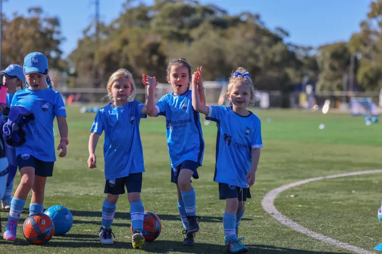 Young girls in Sydney FC kit high-fiving and smiling at a Girls Only Holiday Clinic